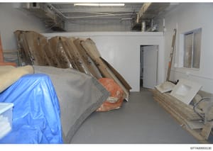 This photograph shows an interior storage or warehouse space containing multiple rolled materials in cardboard tubes, plastic sheeting, and various building or construction materials. The image appears to be documentary evidence from the investigatio