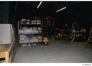 This photograph shows the interior of a storage or maintenance facility, likely connected to one of Epstein's properties. The image documents a garage or warehouse space containing organized shelving units with various boxes and equipment, tools on w