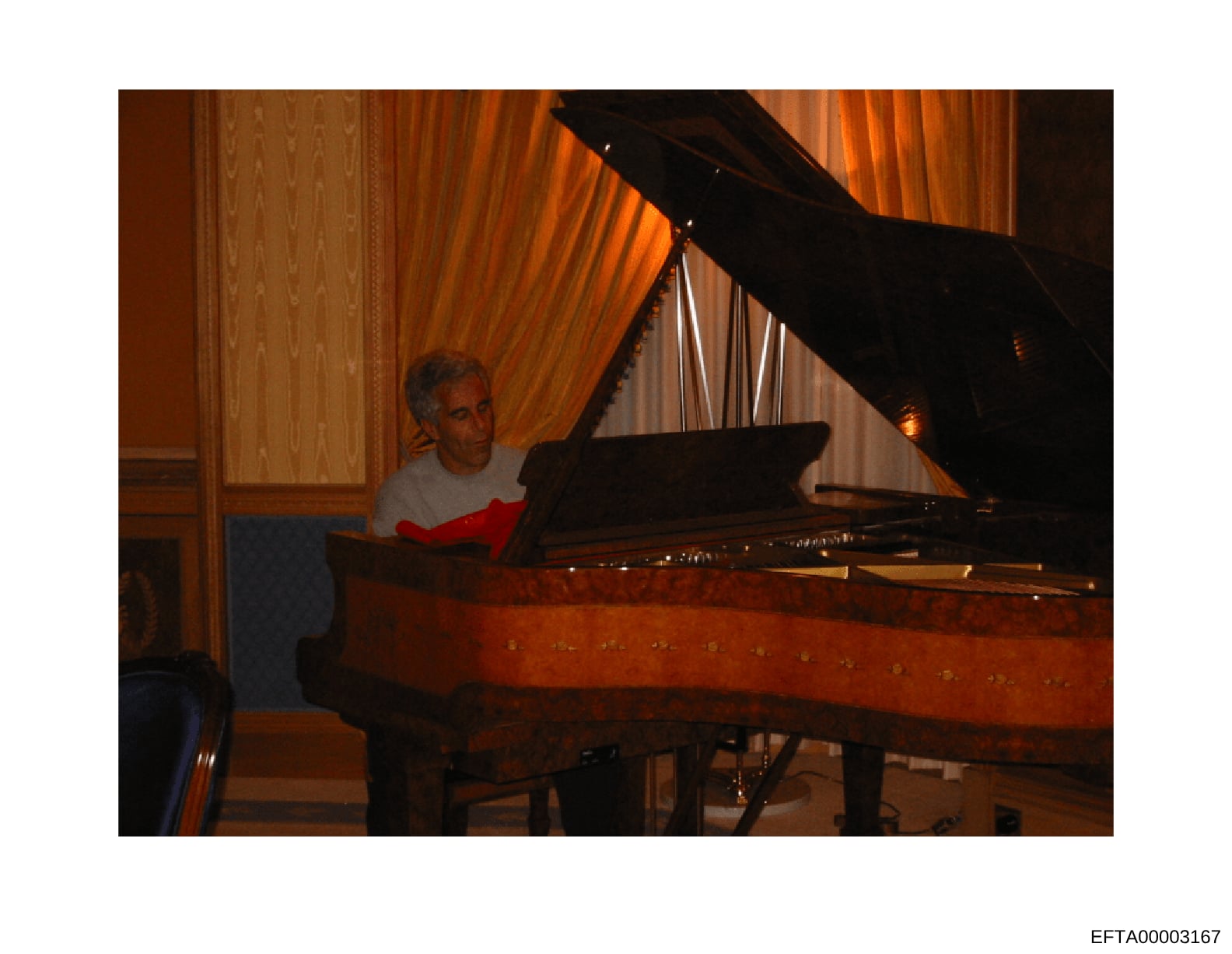 This photograph shows a man seated at a grand piano in an elegantly appointed room with formal drapes and wood paneling. The image appears to be from a residence or formal venue, captured during an evening or indoor setting. The photograph is part of