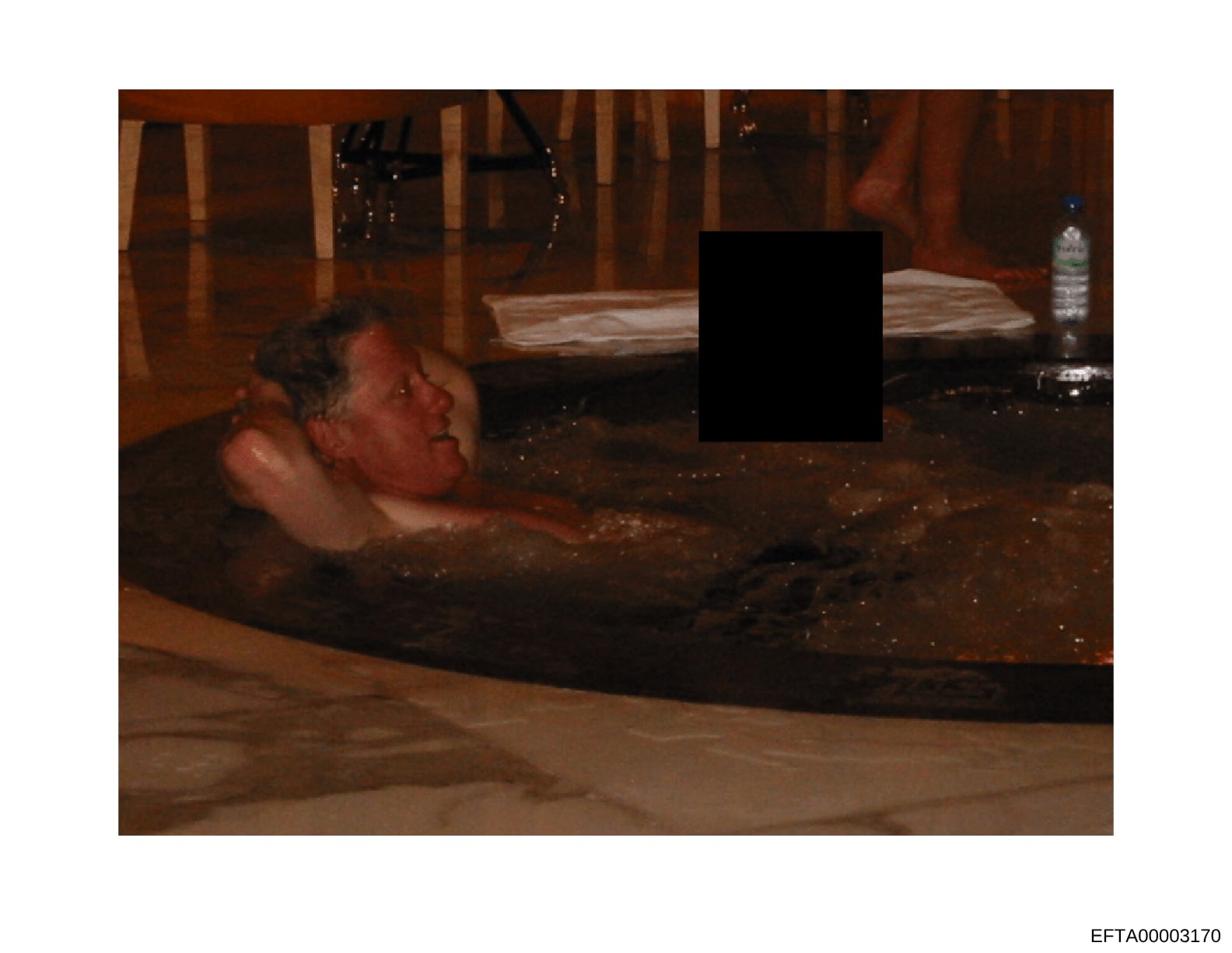 This is an evidence photograph depicting the interior of a residential property, showing a bathing area with warm-toned wooden finishes. A portion of the image containing a person has been redacted with a black rectangle. A water bottle is visible on