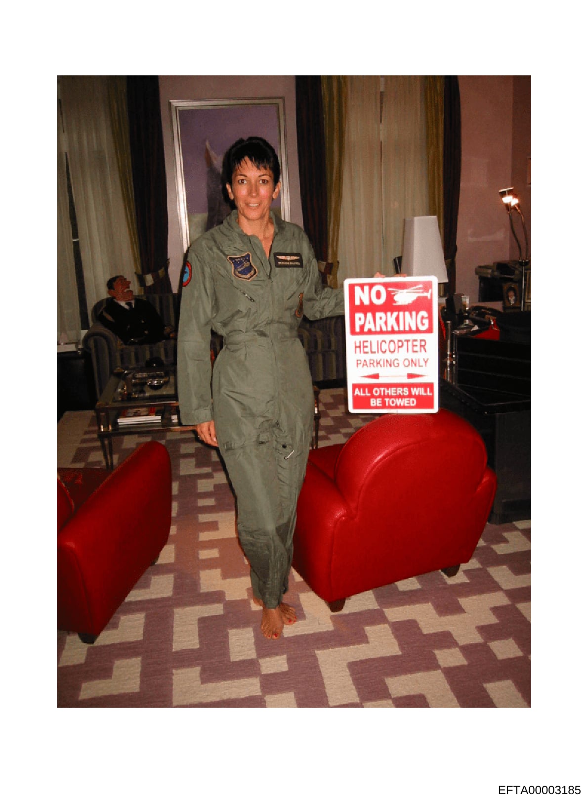 This is a photograph of a woman wearing a U.S. Air Force flight suit with visible rank insignia and patches, standing indoors in what appears to be a formal or social setting. A 'No Parking - Helicopter Parking Only' sign is prominently displayed nex