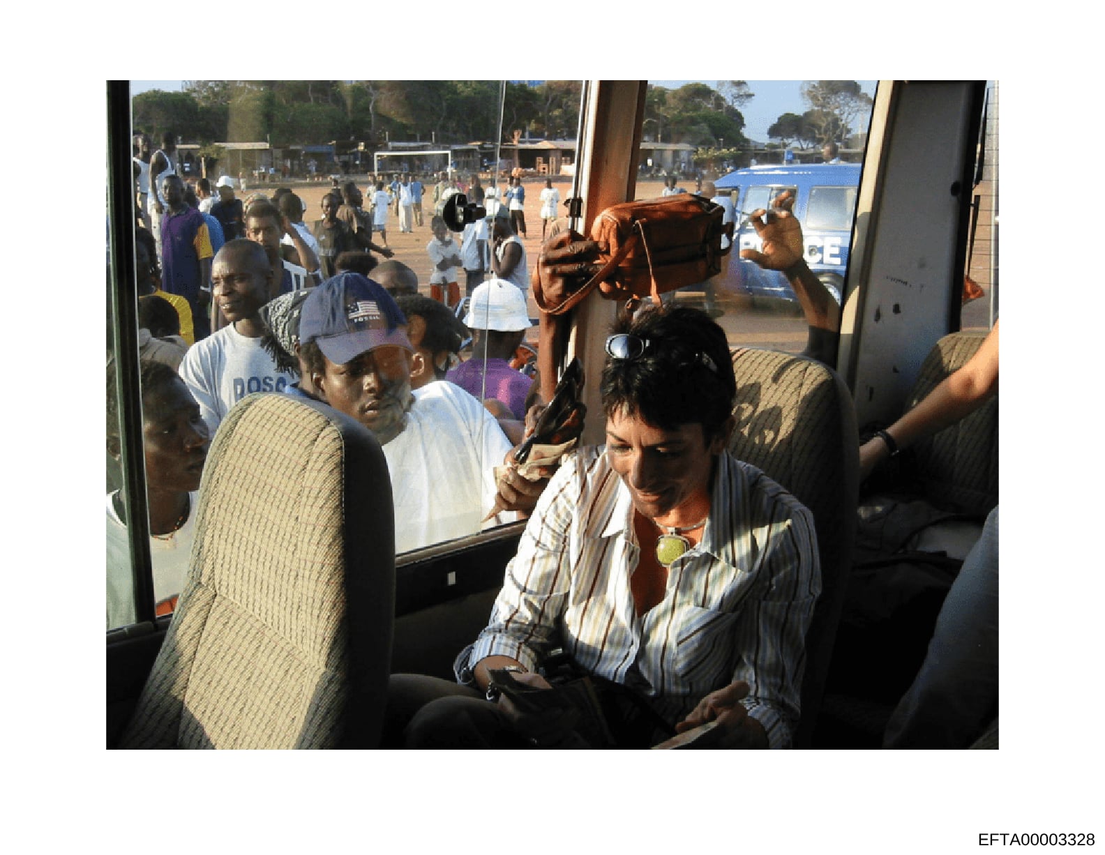 This photograph shows a crowded public event or gathering at what appears to be a sports field or recreational facility. The image captures numerous people both inside what looks like a transport vehicle or viewing area and outside in a large outdoor