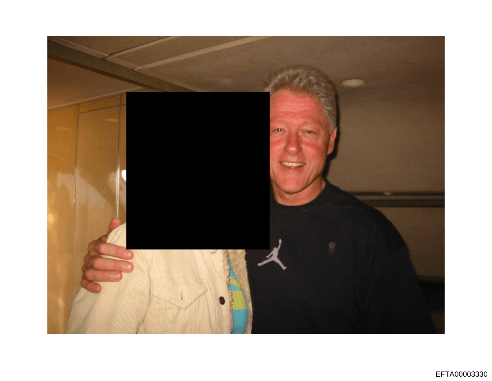 This is an evidence photograph from the Epstein investigation files showing an indoor scene with two individuals. One person is visible on the right side of the frame wearing a black Jordan-branded shirt, smiling at the camera. The other person on th
