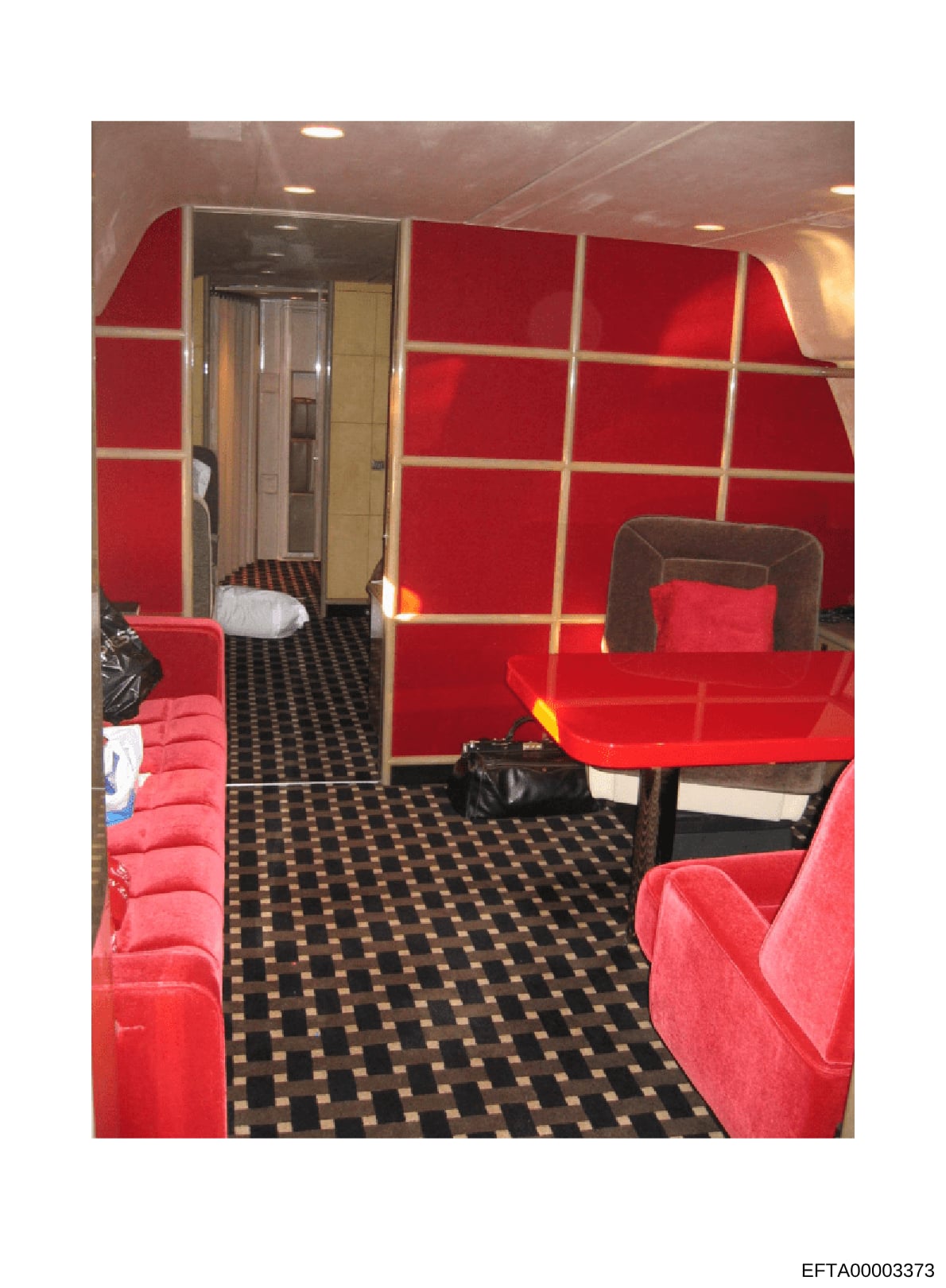 This photograph shows the interior of a private aircraft cabin, featuring red upholstered seating arrangements, a black and gold checkered floor, and beige/tan wall paneling. The image documents the luxury accommodations aboard what appears to be Eps