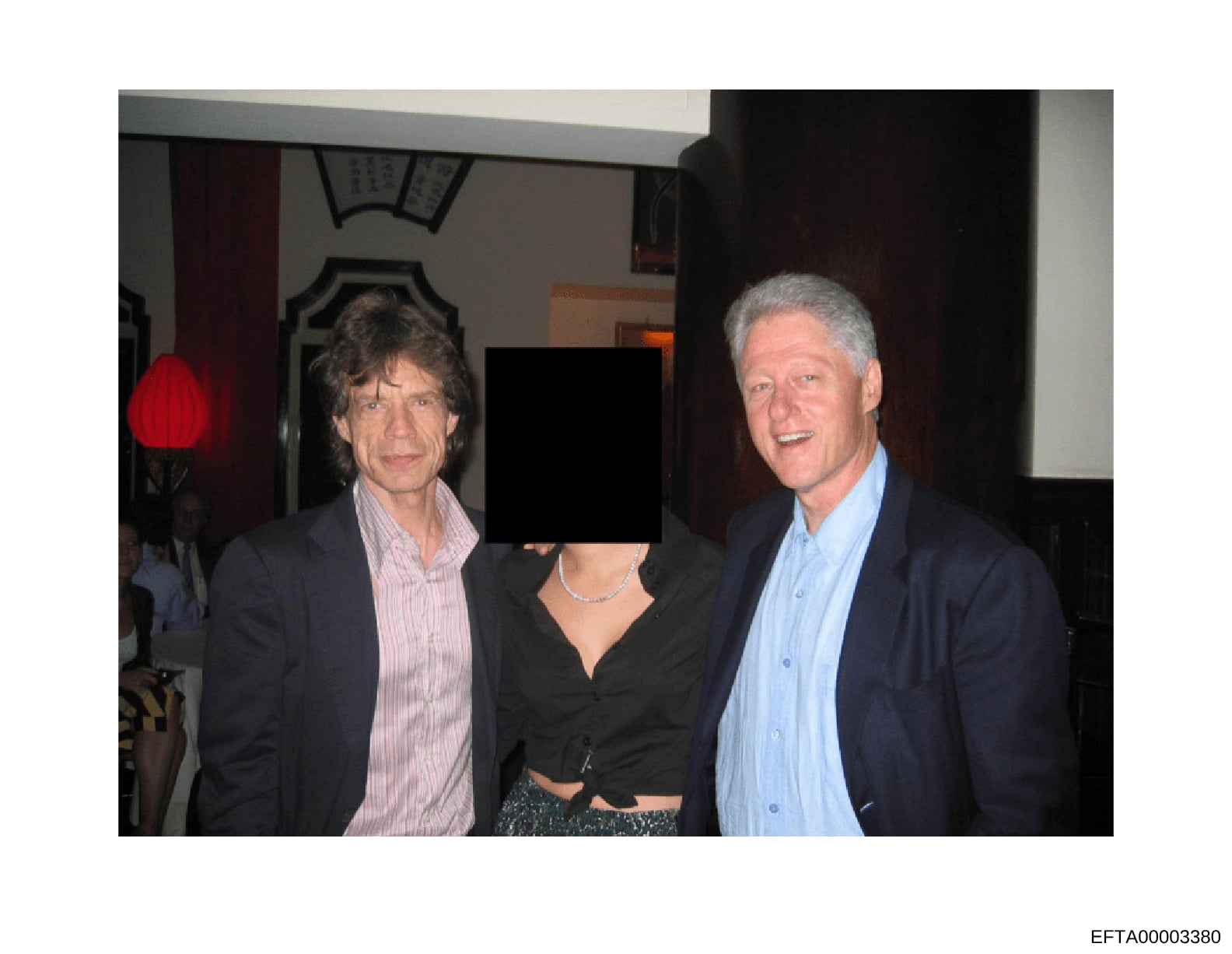This is a photograph taken at an indoor social gathering or event, showing three people posing together in what appears to be an elegant interior space. The identity of the center person has been redacted/obscured. The photo is part of the Epstein in