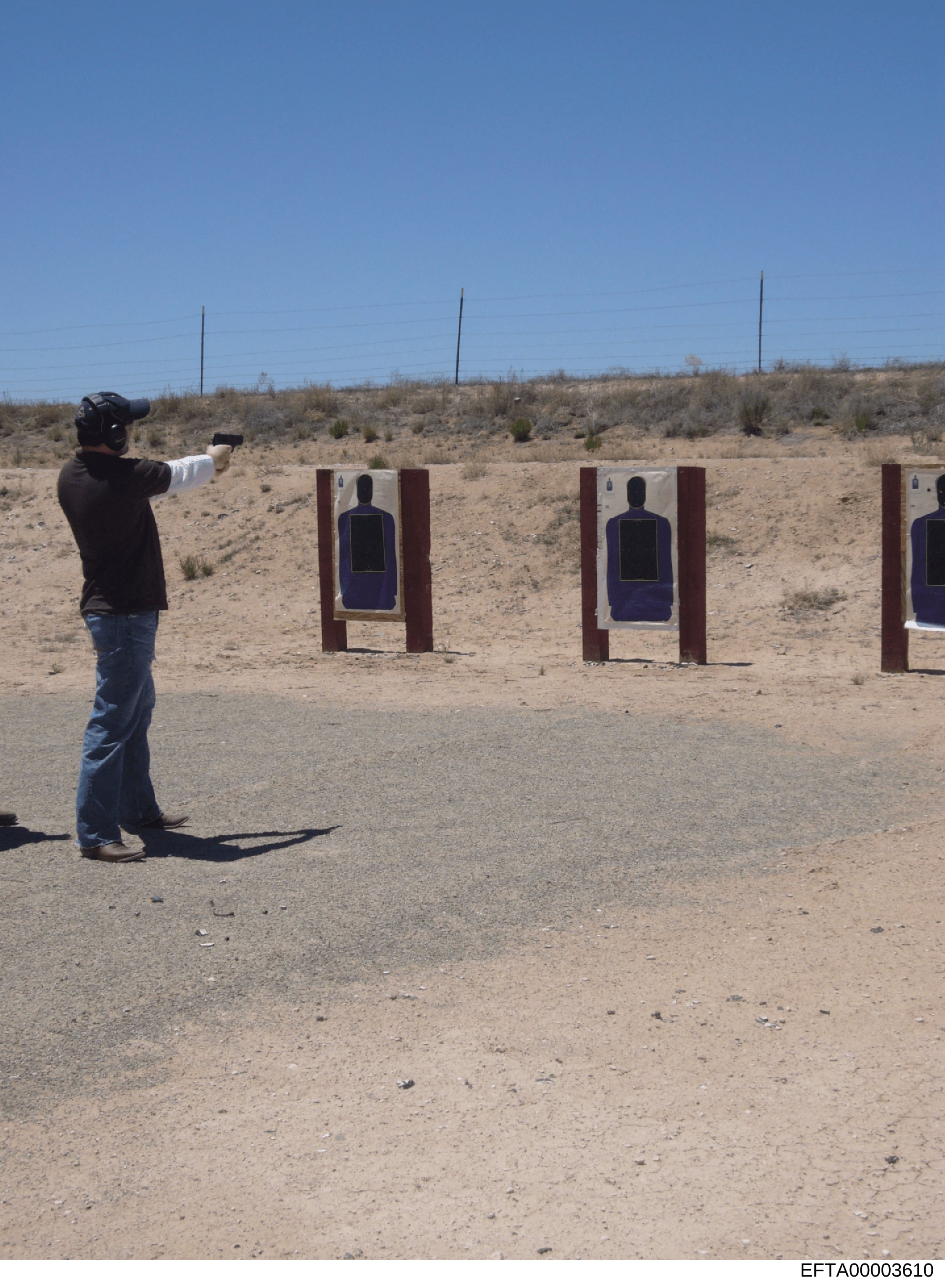 This photograph shows a person engaged in firearms training at an outdoor desert shooting range. The image depicts proper shooting stance and form at what appears to be a professional or law enforcement training facility, with multiple target station