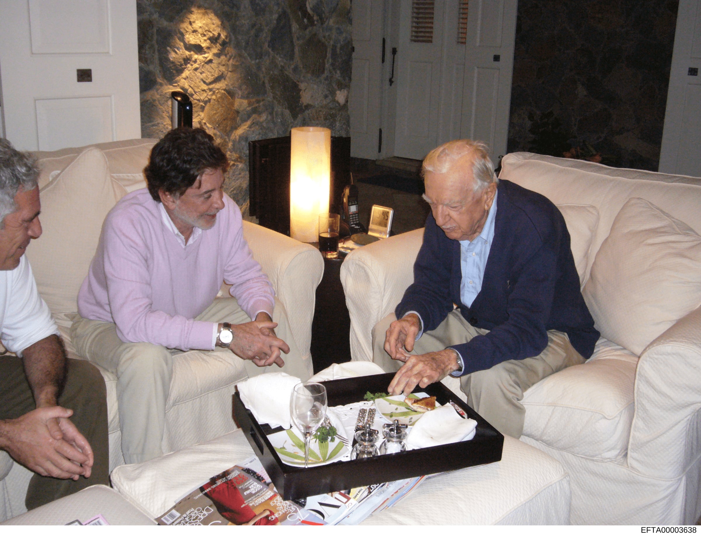 This photograph depicts three men in discussion within a luxuriously appointed interior space, featuring high-end furniture, marble accents, and professional lighting. The setting appears to be a formal living room or meeting area at an upscale prope
