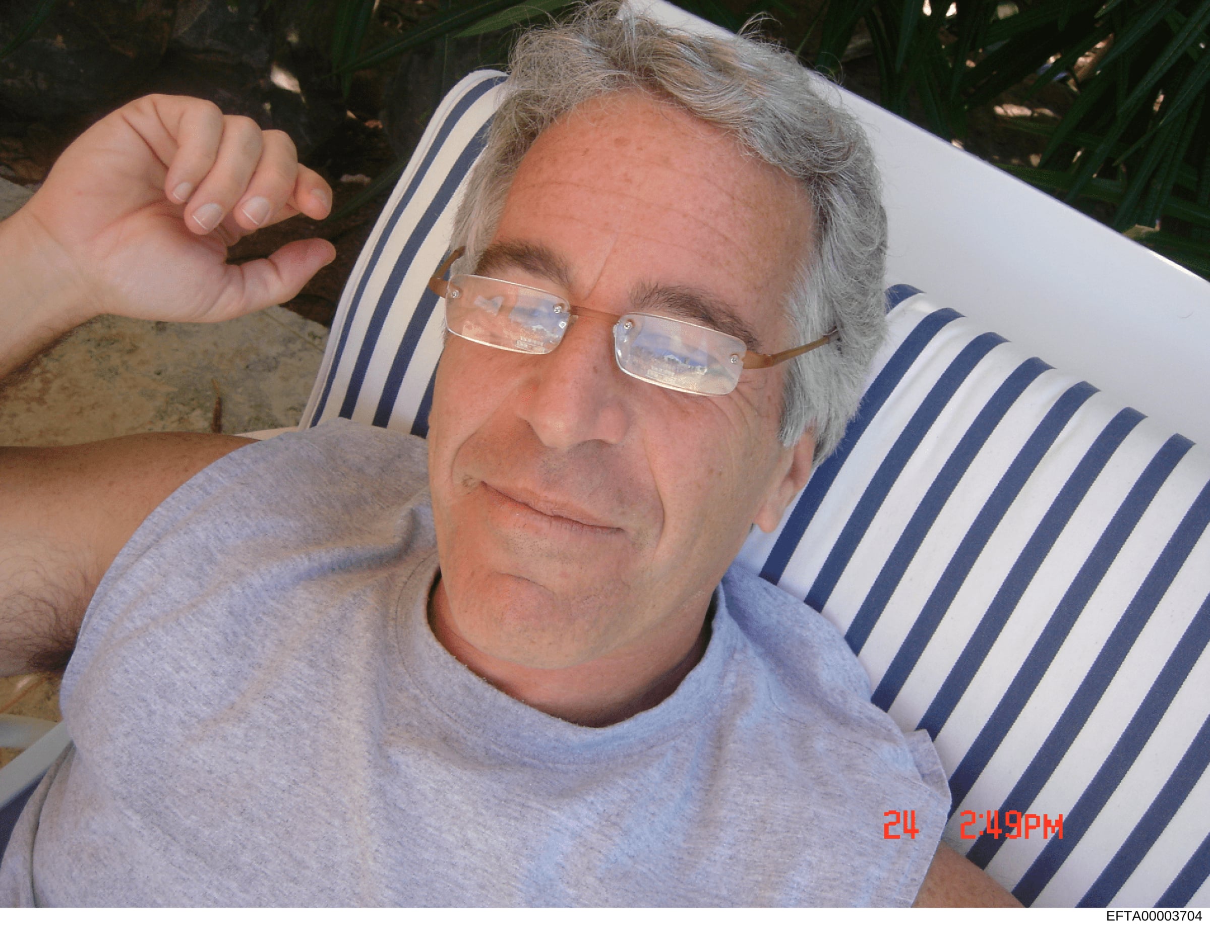 This is a casual personal photograph showing a middle-aged man wearing glasses and a light-colored shirt, resting against a striped pillow or cushion outdoors. The image appears to be dated 2004 based on the timestamp visible in the lower right corne