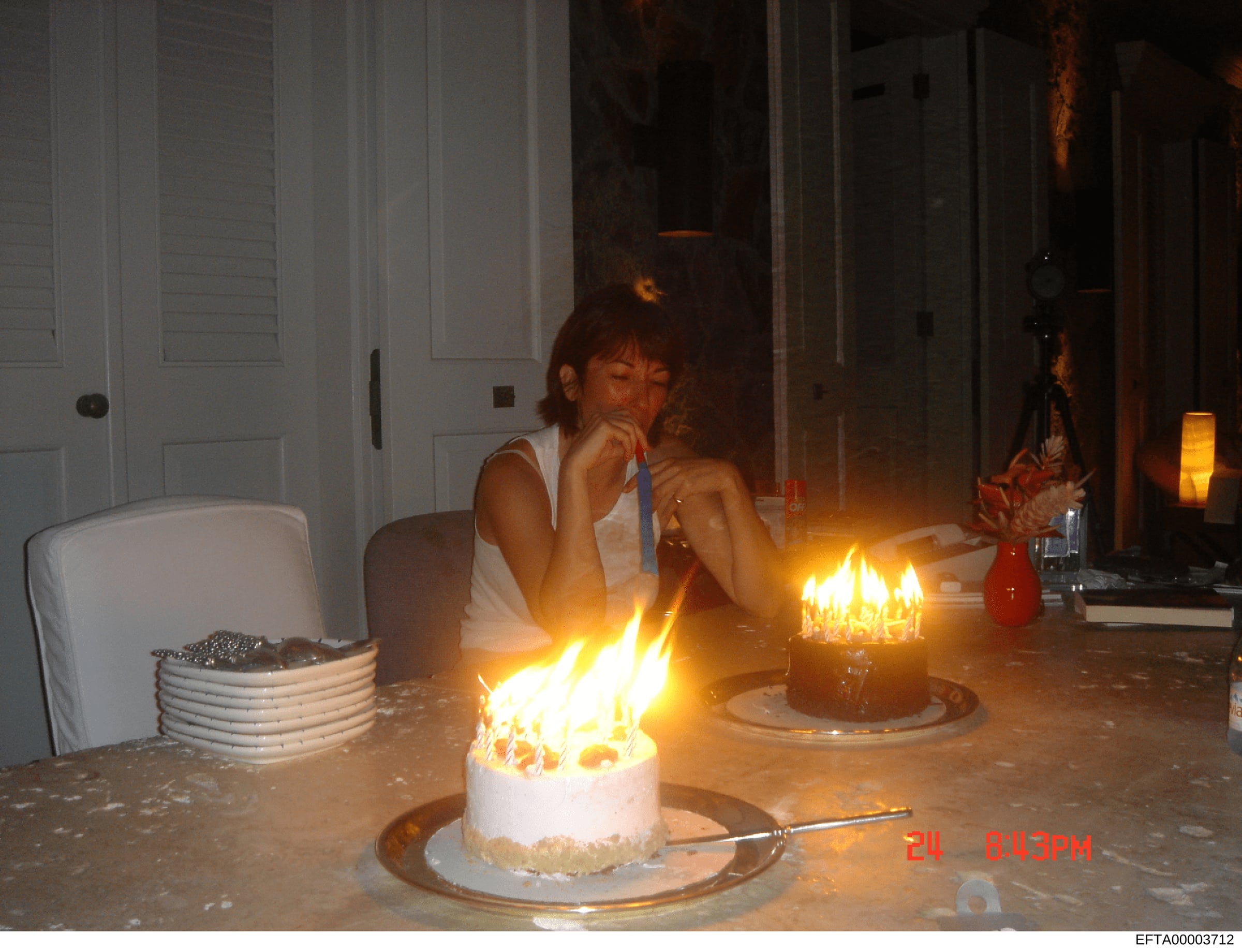 This is a casual photograph showing an interior domestic scene with a person seated at a table with lit birthday cakes. The image appears to be from a personal collection or surveillance file, dated in the early 2000s based on the timestamp visible (