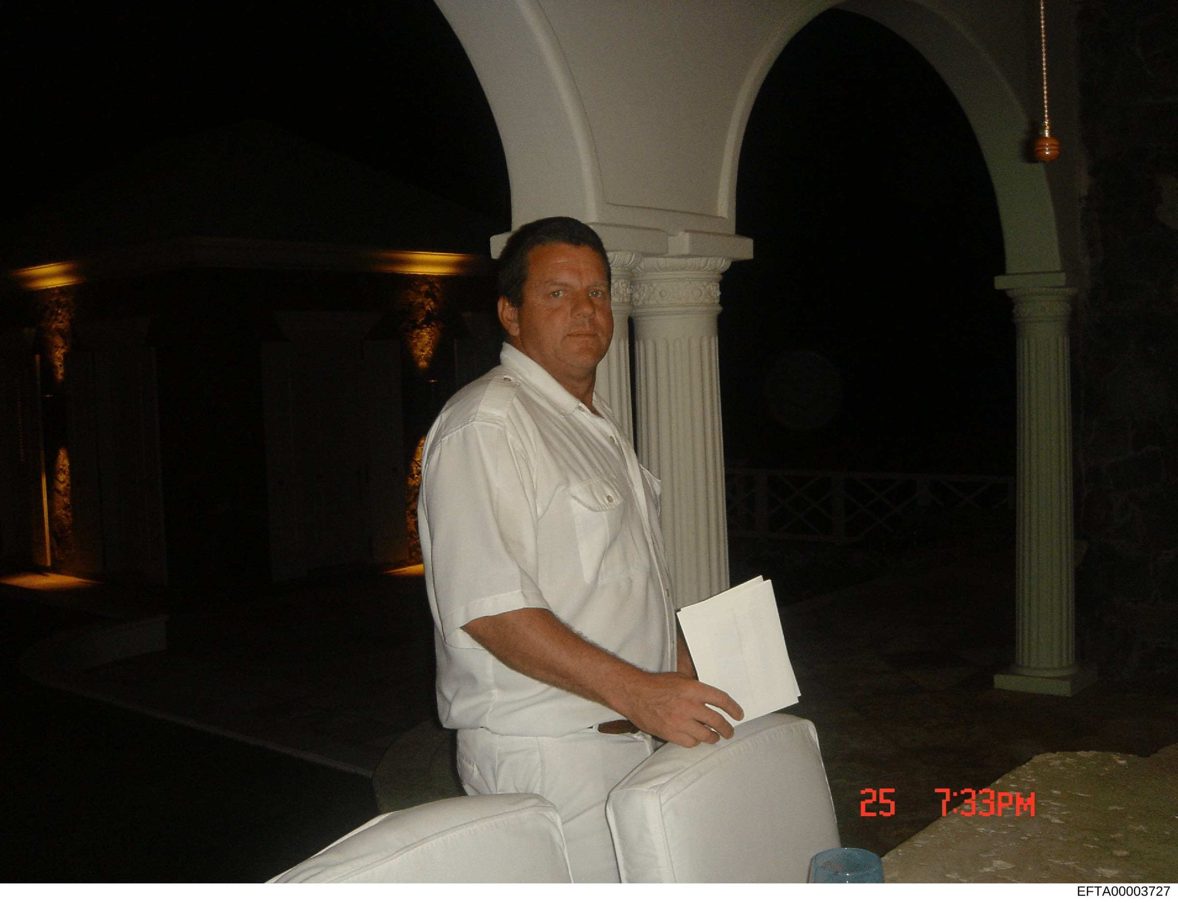 This is an evidence photograph showing a man in white clothing sitting in what appears to be an upscale interior space with neoclassical architectural features including white columns and arched doorways. The photo is timestamped 7:33 PM on the 25th 