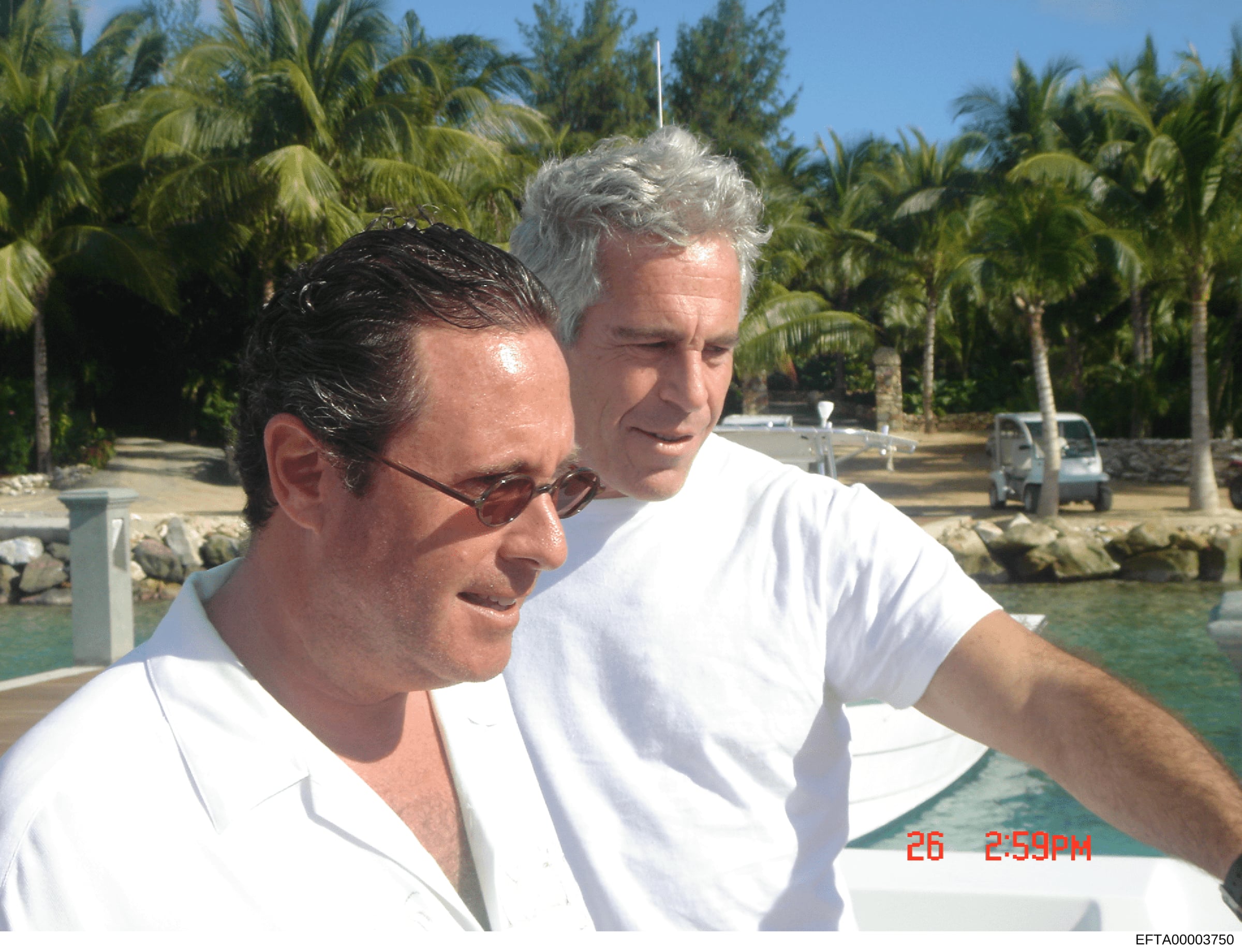 This is a photograph showing two men on a boat in a tropical waterfront setting with palm trees visible in the background. The photo appears to be from the Epstein investigation files and was taken on 26th (date stamp visible as '26 2:59PM'). The ima