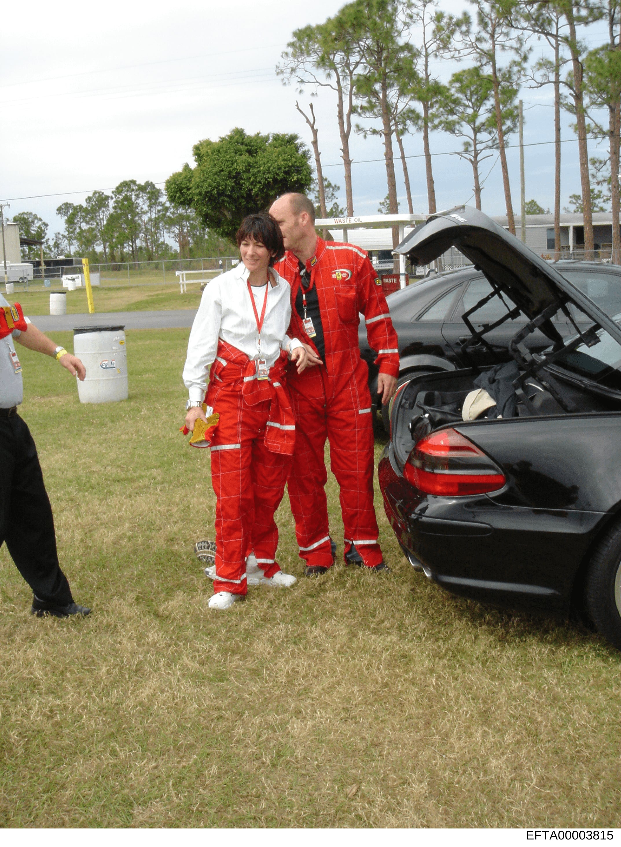 This photograph shows two individuals at what appears to be an emergency response or hazmat training event. A woman in a white jacket and red protective suit stands next to a male instructor or official also wearing a red protective suit with reflect