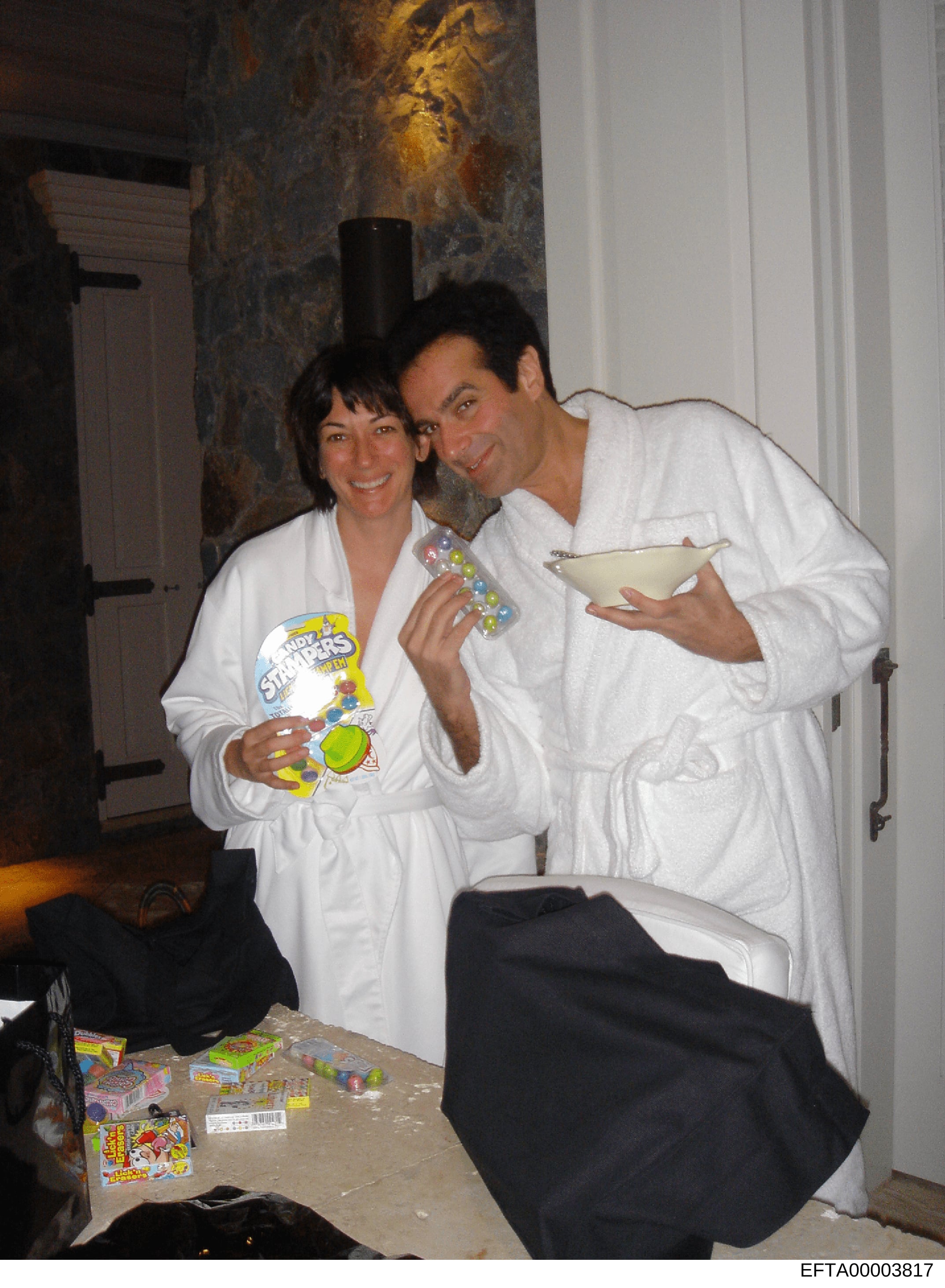 This is a casual photograph showing two people in white robes at what appears to be a private indoor event or party. The image shows them posing together while holding beverages and game boxes, with various items scattered on a table in front of them