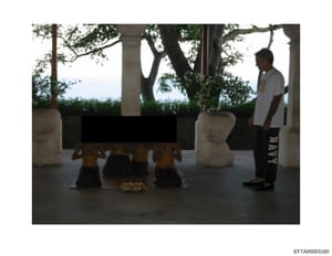 This is an evidence photograph showing an interior/covered terrace area of a property, featuring a waterfront view, mature trees, decorative planters, and a man standing on the right side of the frame. The image appears to document the property's lay