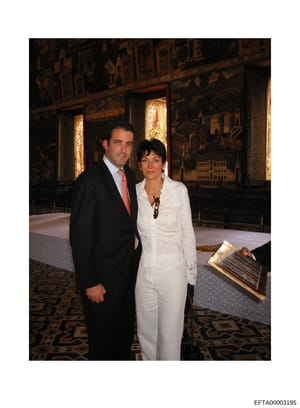 This photograph shows two people posing together at what appears to be a formal event or gathering in an elegant, richly decorated interior space. The setting features ornate gold-leafed panels with Asian architectural motifs and detailed landscape s