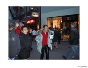 This photograph shows a nighttime street scene with multiple people gathered outside a storefront marked 'SAM BAR.' The image appears to be surveillance or investigative documentation, capturing individuals on a public street in what looks like a com