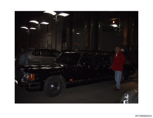 This is an evidence photograph showing a black limousine parked on a nighttime street in an urban setting. The image captures what appears to be an investigation-related documentation of a vehicle, with several individuals visible near the car. The p