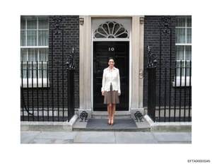 This is a color photograph showing a woman standing on the steps in front of the iconic black door marked with the number '10' at 10 Downing Street in London. The photo captures the famous entrance to the British Prime Minister's residence, with its 