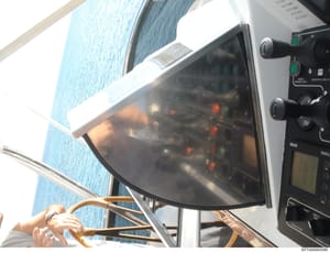 This photograph shows the navigation and control systems aboard a vessel, featuring a marine electronic display screen with illuminated indicators and a control panel with multiple switches and gauges. The image captures navigation equipment typicall