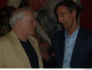 This photograph shows two men engaged in conversation at what appears to be an indoor social or professional event. The image quality and color palette suggest it was taken in the 1990s or early 2000s. One man wears a yellow blazer over dark clothing