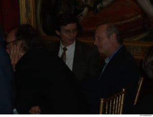 This is an evidence photograph from the Epstein investigation showing three men in business attire conversing indoors. The setting appears to be an upscale interior with ornate wooden paneling and gilt-framed artwork visible in the background. The ph