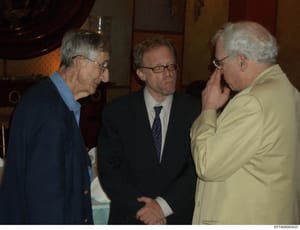 This photograph depicts three men engaged in conversation at what appears to be an indoor formal or social event. The image shows three older gentlemen in business attire conversing in what looks like a reception or gathering space. Without additiona