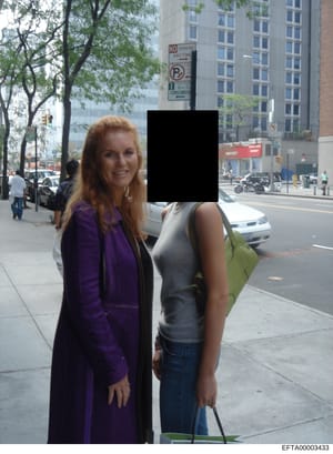 This is a candid photograph taken on a city street showing two women posing together. One woman wears a purple jacket and has reddish-blonde hair; the other wears a gray sleeveless top and blue jeans, with her face redacted in black. The photo appear