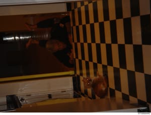 This is an evidentiary photograph of an interior room featuring a distinctive black and tan/beige checkered wall pattern. The image shows a partial view of what appears to be a residential space with minimal furnishings visible. The photograph is tak