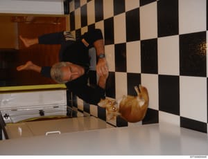 This is a photograph of an older man in dark clothing posing in a modern kitchen featuring distinctive black and white checkered tile flooring. The image appears to be taken in one of Jeffrey Epstein's residences and is part of the investigative evid