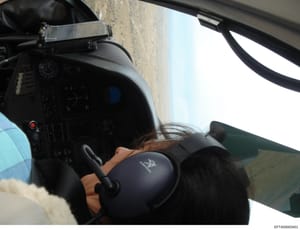 This is an evidence photograph showing the interior cockpit of a helicopter in flight, with a pilot visible at the controls. The image captures the instrument panel, control stick, and overhead systems. This photo likely documents aircraft used in th
