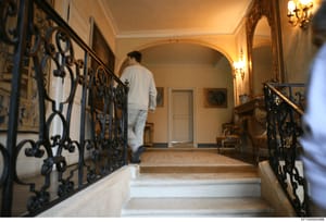 This is a photograph of an ornate interior stairwell in what appears to be a luxury residential property associated with the investigation. The image shows elegant architectural details including decorative iron railings, wall sconces, and classical 