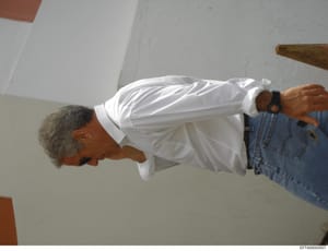 This is a photograph showing a man with gray hair wearing a white long-sleeved shirt and blue denim jeans, photographed from above at an angle. The image appears to be taken indoors against white/gray walls. The photograph's purpose in the investigat