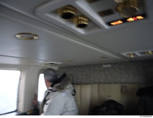 This photograph shows the interior ceiling and cabin of a private aircraft, featuring brass fixtures, recessed lighting, and an illuminated overhead sign. One person is visible in the cabin. The image appears to be evidence documentation from the Eps