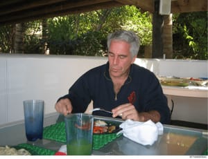 This is a personal photograph showing a middle-aged man with gray hair dining outdoors on what appears to be a covered patio or veranda. The setting includes tropical vegetation in the background, suggesting a warm-weather location. The image was sei