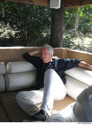 This is a photograph showing a man with gray hair relaxing on a cushioned outdoor sofa or daybed in a tropical setting. The image appears to be from an estate or property with lush vegetation visible in the background. The photograph is part of the E