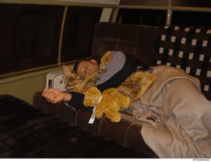 This is a personal photograph showing an individual resting in what appears to be the back seat of a vehicle, holding a mobile device and a yellow stuffed animal. The photo was recovered from the Epstein investigation files and may be relevant to est