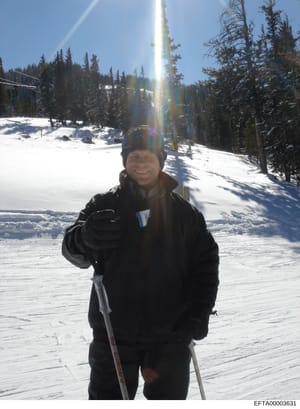 This is a personal photograph taken at a ski resort showing an individual in winter skiing attire on a snowy mountain slope. The image appears to be a casual recreational photo taken during daytime in clear weather conditions. While the photograph it