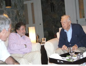 This photograph shows three men engaged in conversation in an elegantly appointed interior space with marble walls, modern furniture, and table settings. The setting appears to be a high-end residential property, likely documenting a social gathering