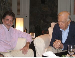 This is a photograph showing two men seated together in what appears to be an upscale residential interior. The image captures an informal social moment in a living room or lounge area. The photograph is part of the Epstein investigation files and ma