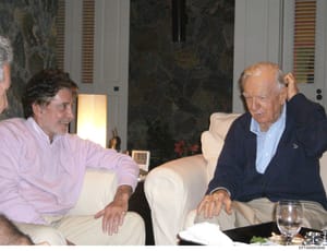 A photograph showing two men in casual conversation within an upscale interior space, featuring marble walls, modern furnishings, and table settings. The image appears to be documentation from a private residence or social gathering and is included i