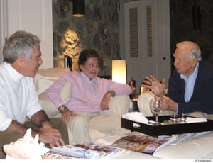 This photograph captures three men in conversation within what appears to be a high-end residential interior space. The setting features luxury finishes including dark marble walls, designer lighting, and upscale furnishings. The image appears to be 