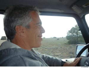 This is a candid photograph taken inside a vehicle showing a middle-aged man with gray hair at the steering wheel, driving on a rural road with open fields and trees visible in the background. The photo appears to be documentary evidence, possibly ta