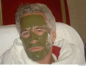 This is a candid photograph showing a man with gray hair wearing a green/olive-colored face mask or spa treatment. The image appears to be a personal or casual photo taken in an indoor setting with red drapes visible in the background. The photograph