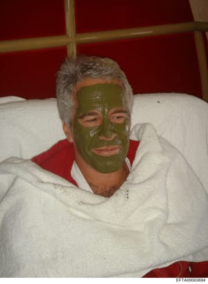 This is a personal photograph showing a man with gray/white hair wearing a green facial mask, lying on a bed with white pillows and red bedding. The image appears to be a casual personal photo, possibly taken at a residential property. The relevance 