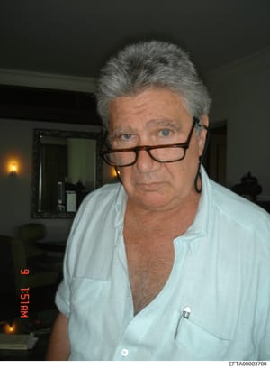 This is a personal photograph of a middle-aged man with gray hair wearing glasses and a light blue shirt, taken indoors. The image appears to be documentary evidence collected as part of the investigation, though the subject's identity is not indicat