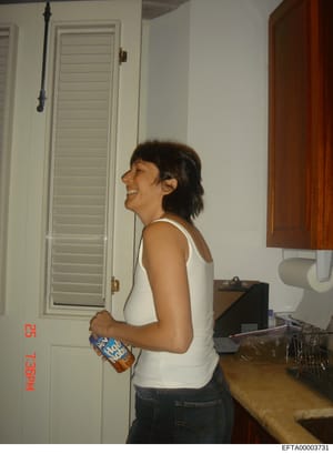 This is a personal photograph showing a woman in a kitchen setting. The image appears to be from a residential property and is marked with an EFTA evidence identifier, indicating it was collected as part of the Epstein investigation. The photo docume