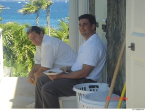 This is a casual photograph taken on December 20, 2003, showing two men in white shirts sitting outdoors on what appears to be a covered patio or balcony with an ocean view. The setting suggests a residential property, with palm trees visible and bri