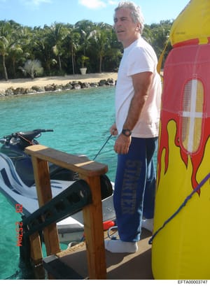 This photograph shows Jeffrey Epstein standing on a boat or dock in clear turquoise water in what appears to be a tropical location. He is wearing casual attire (white t-shirt, dark pants) and is positioned near water sports equipment including jet s