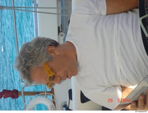 This is a candid photograph taken on a yacht or boat in March 2006, showing a woman with gray hair wearing white clothing and yellow earrings, photographed against a bright blue water background. The image appears to be personal documentation, possib