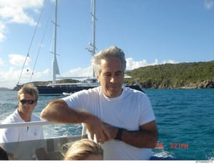 This is a personal photograph showing an older man with gray hair wearing a white t-shirt on a boat, with a large luxury sailing yacht visible in the background. A second person wearing sunglasses is partially visible to the left. The photo appears t